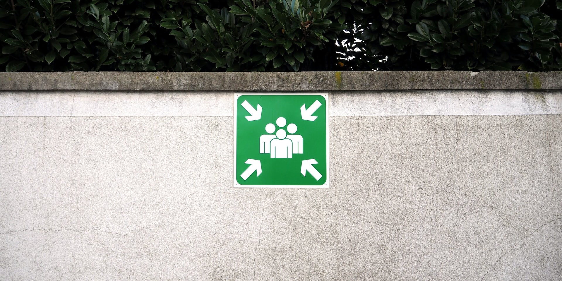 green assembly area sign on a white concrete wall
